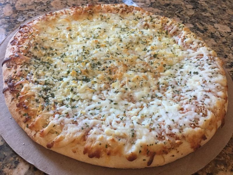 Photo of a cheese pizza with a flaky crust and some seasonings.